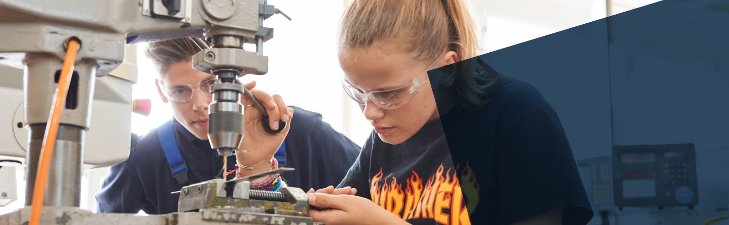 Schülerin und Azubi arbeiten an einer Standbohrmaschine und bohren