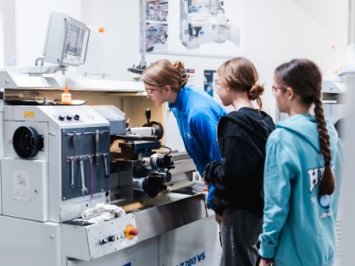 Azubi und Schüler*innen stehen vor Maschine und überprüfen diese